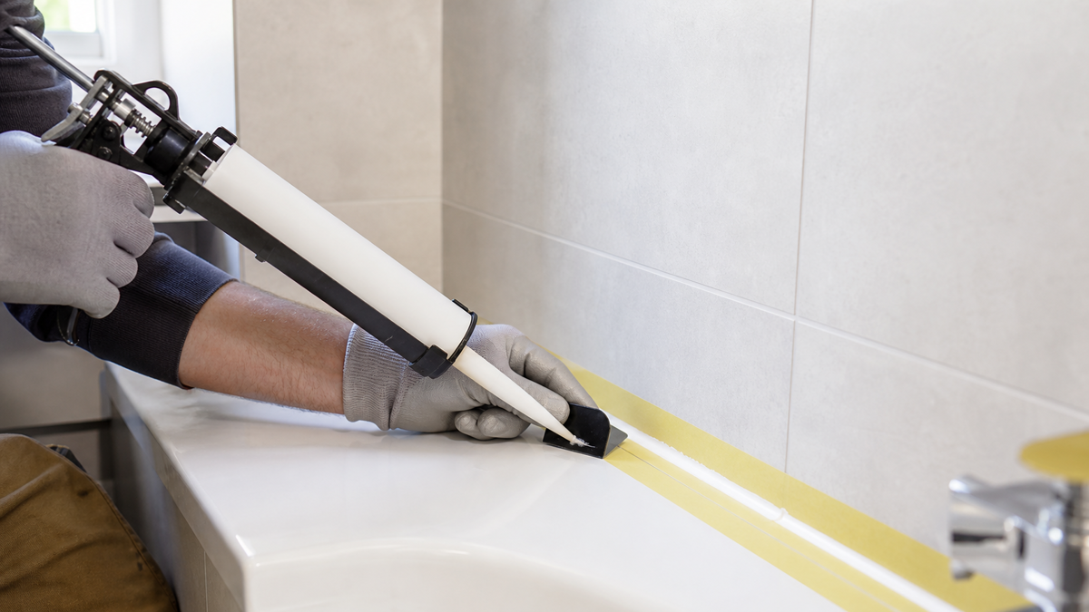 Cartouche de silicone sanitaire appliquée dans un angle sec avec ruban et spatule de lissage